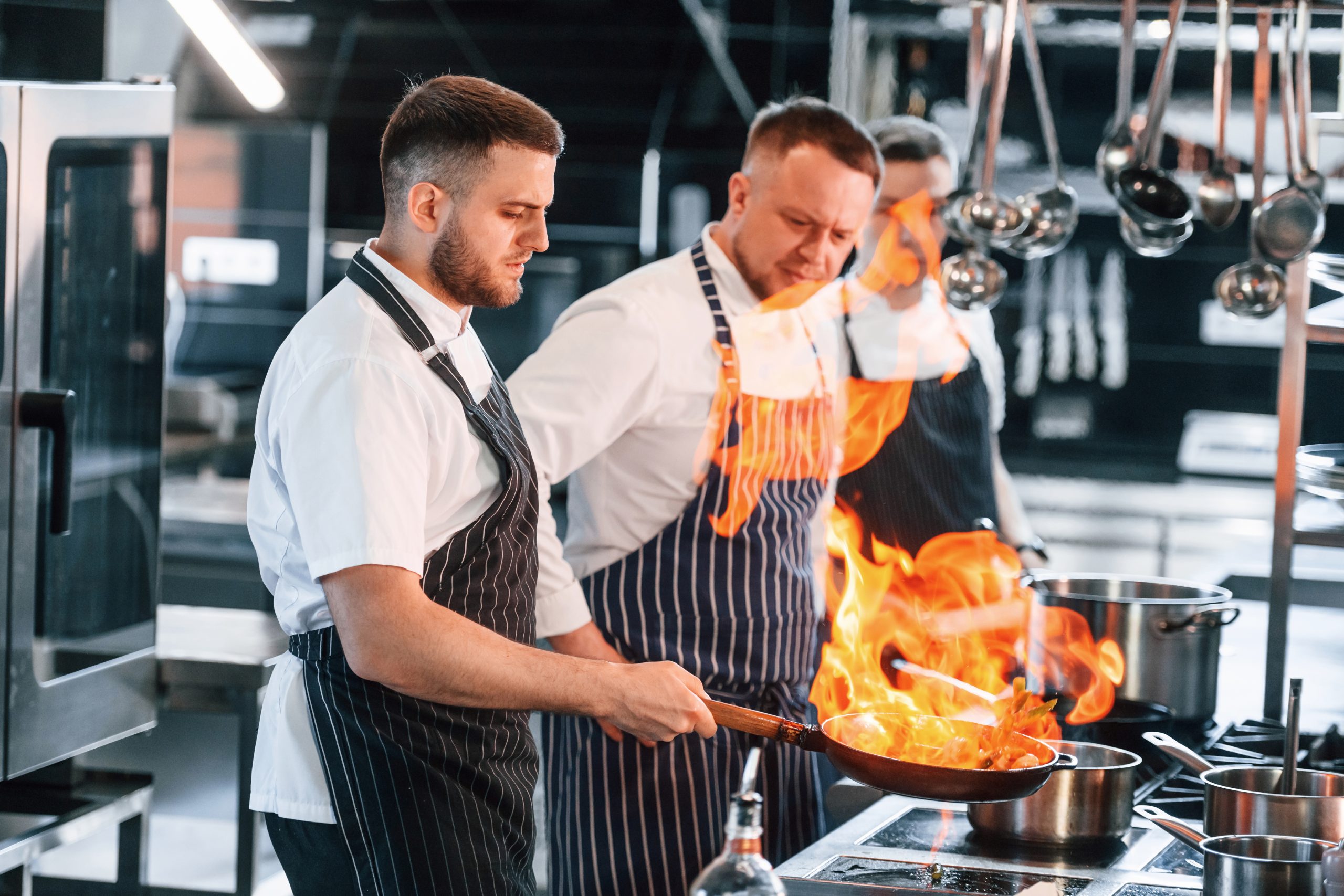 Chef formateur enseignant des techniques culinaires à un apprenti dans une cuisine équipée.